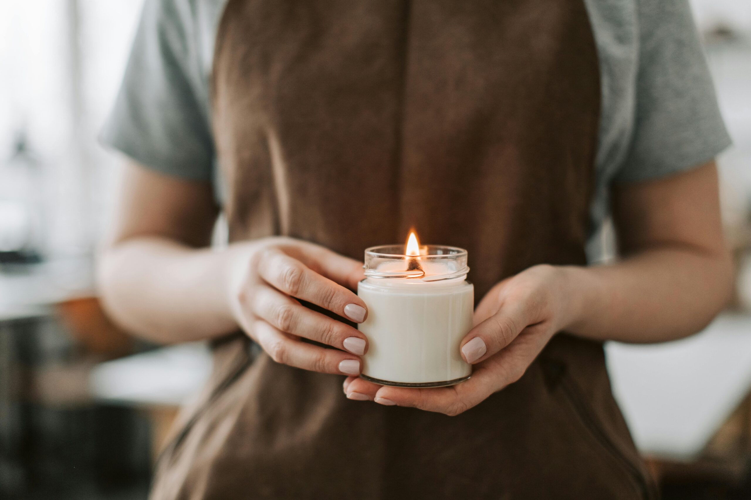 Close-up of hands holding a lit handmade candle in a workshop setting, symbolizing craftsmanship.